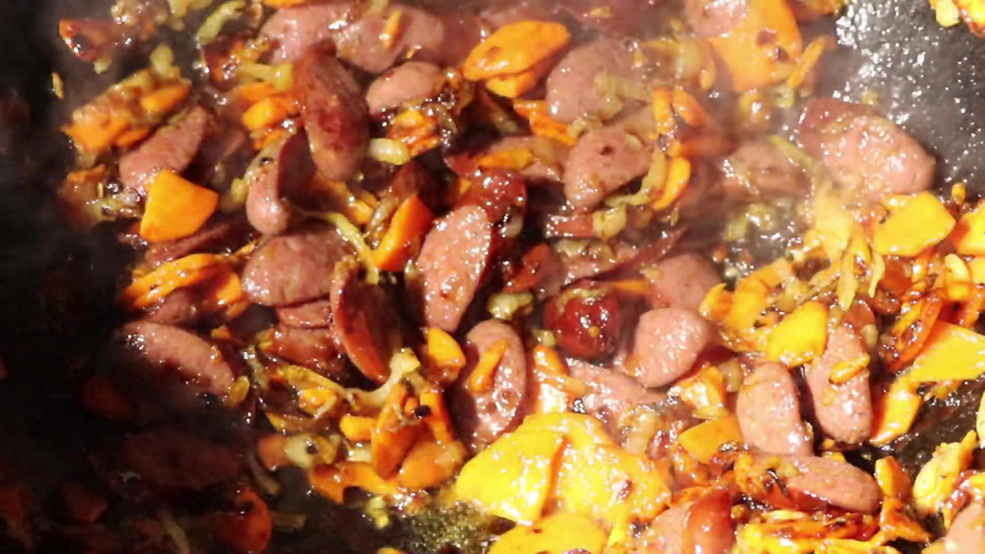 Step 6. Add coarsely chopped hunting sausages to the vegetables and fry for 5-7 minutes. Fried potatoes in a kazan over the fire