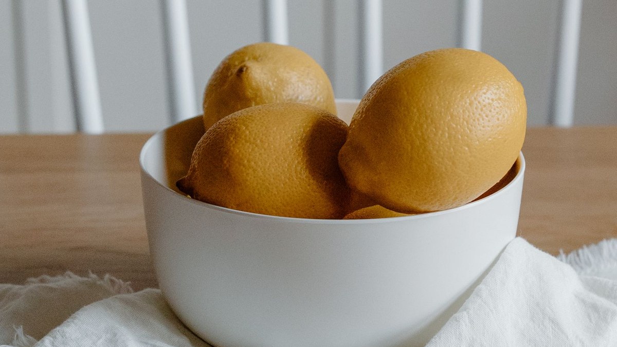 White bowl of lemons on a wooden table with a linen napkin